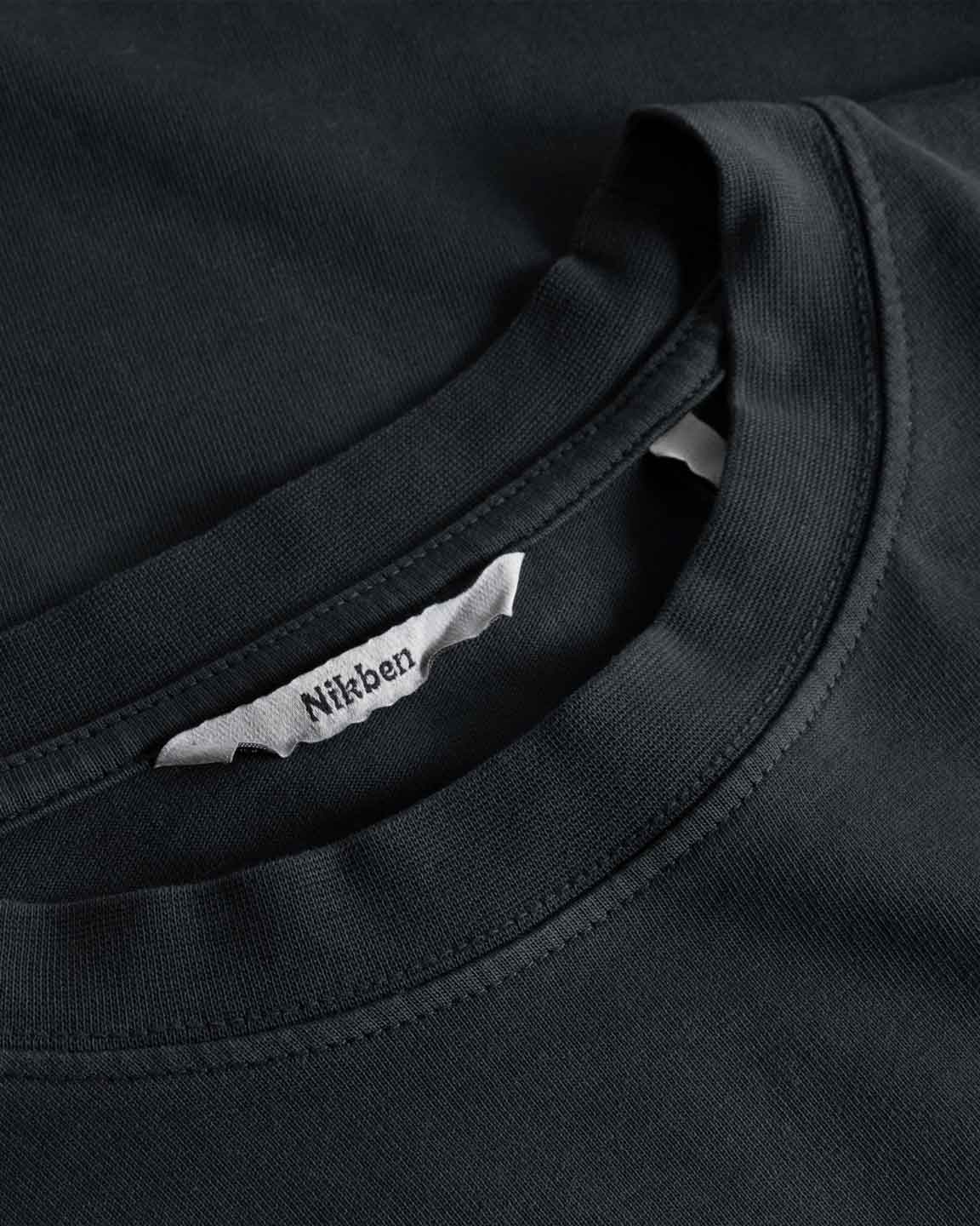 Close-up view of neck label, round neck, and tonal stitchings on a black garment dyed t-shirt