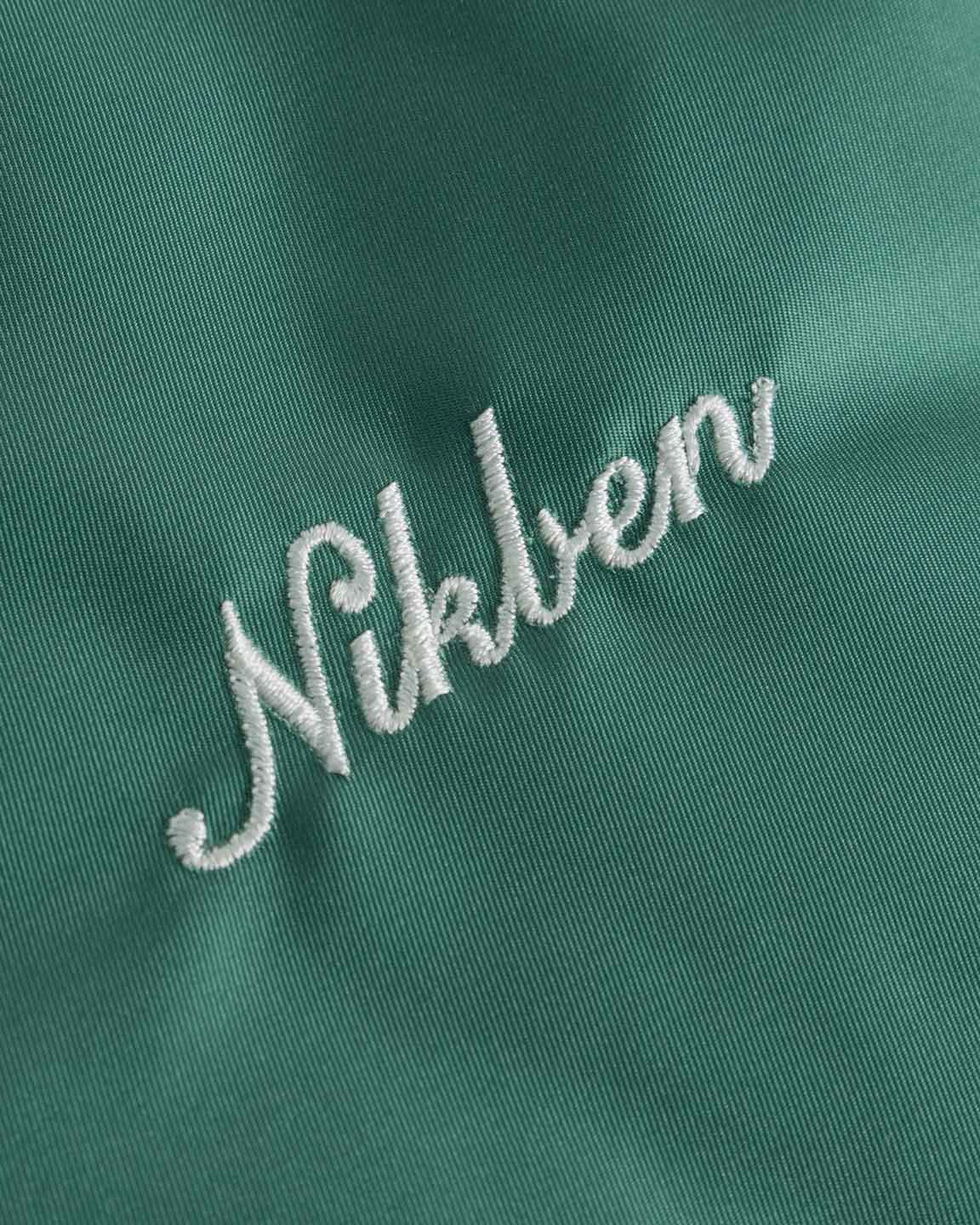 Close up of embroidered script logo on a green 80s style baseball jacket