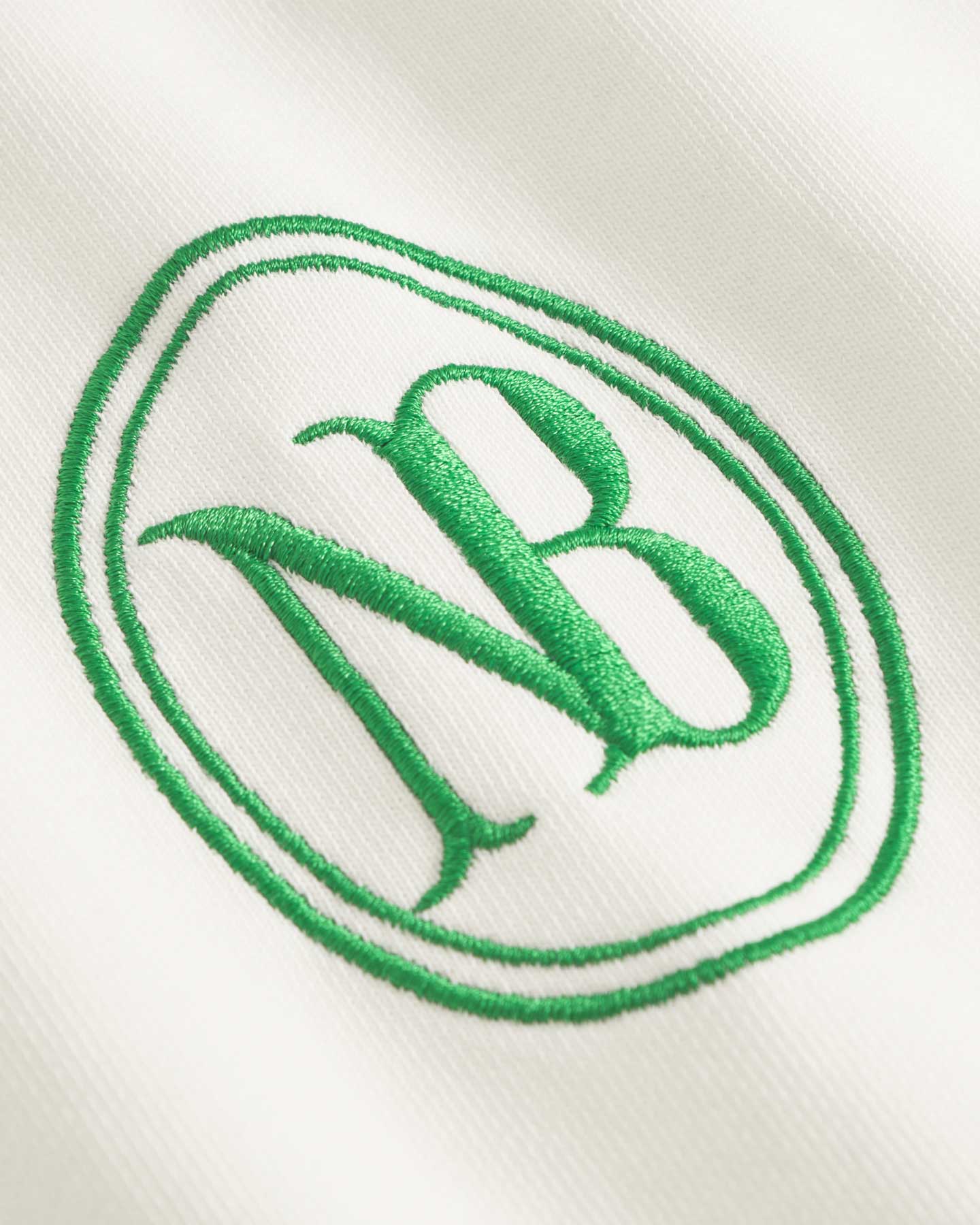 Close up of green NB embroidery on a white and green long sleeved polo shirt 