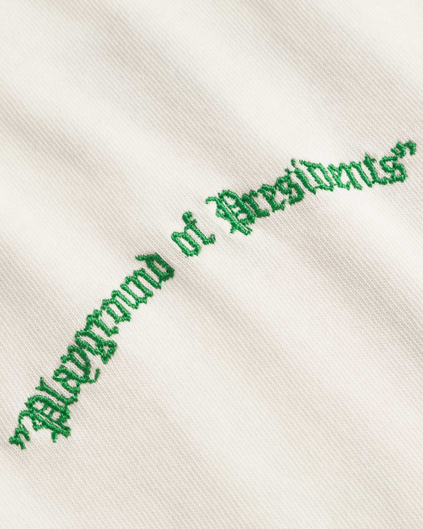 Close up of green embroidery on a cream colored t-shirt