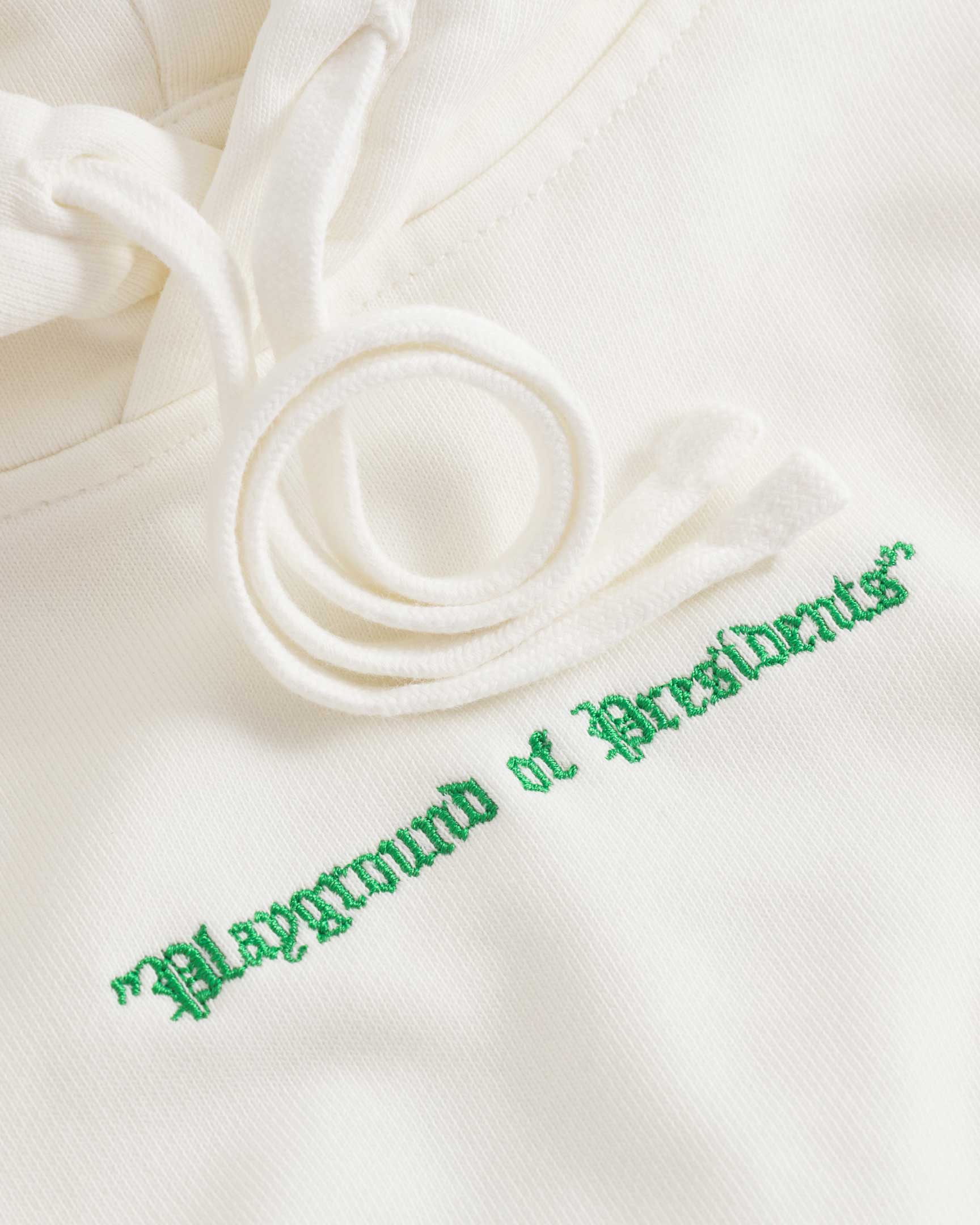 Close up of drawstrings and green embroidery on a cream colored hoodie