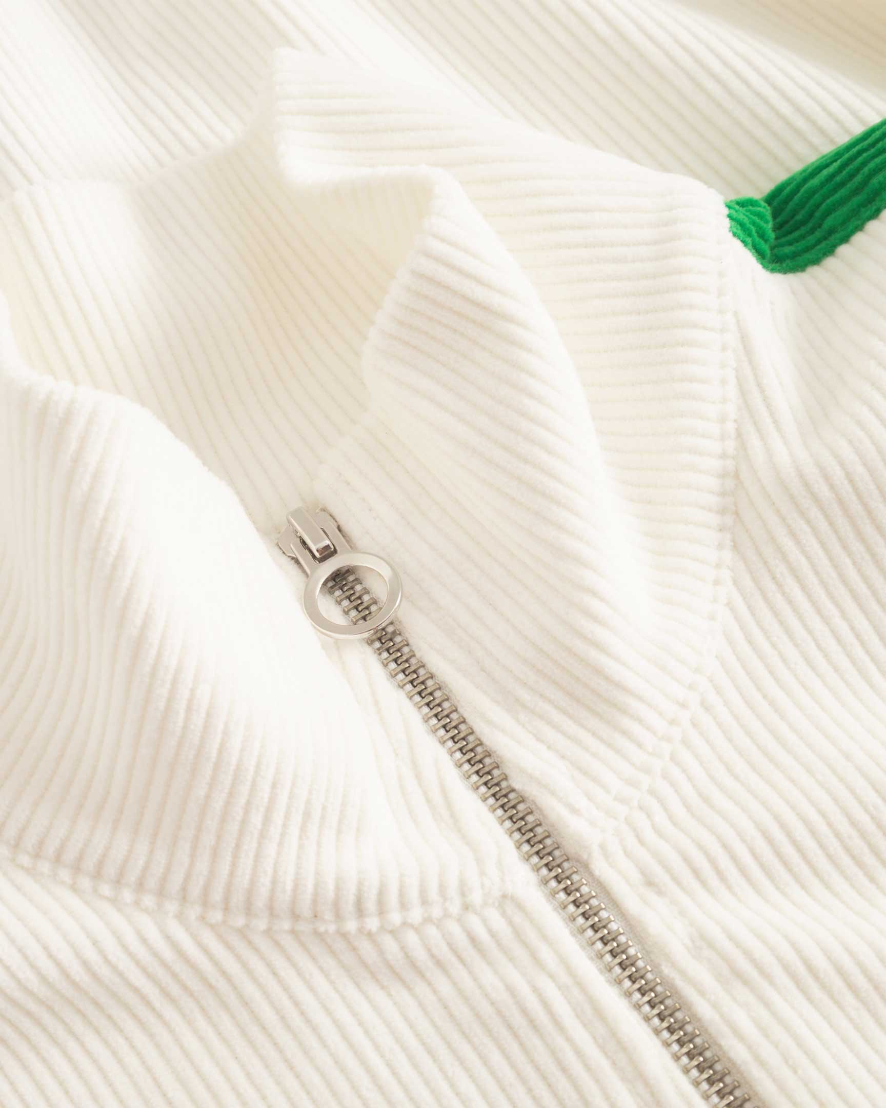 Close up of zipper on a white and green corduroy track suit jacket with NB embroidery 