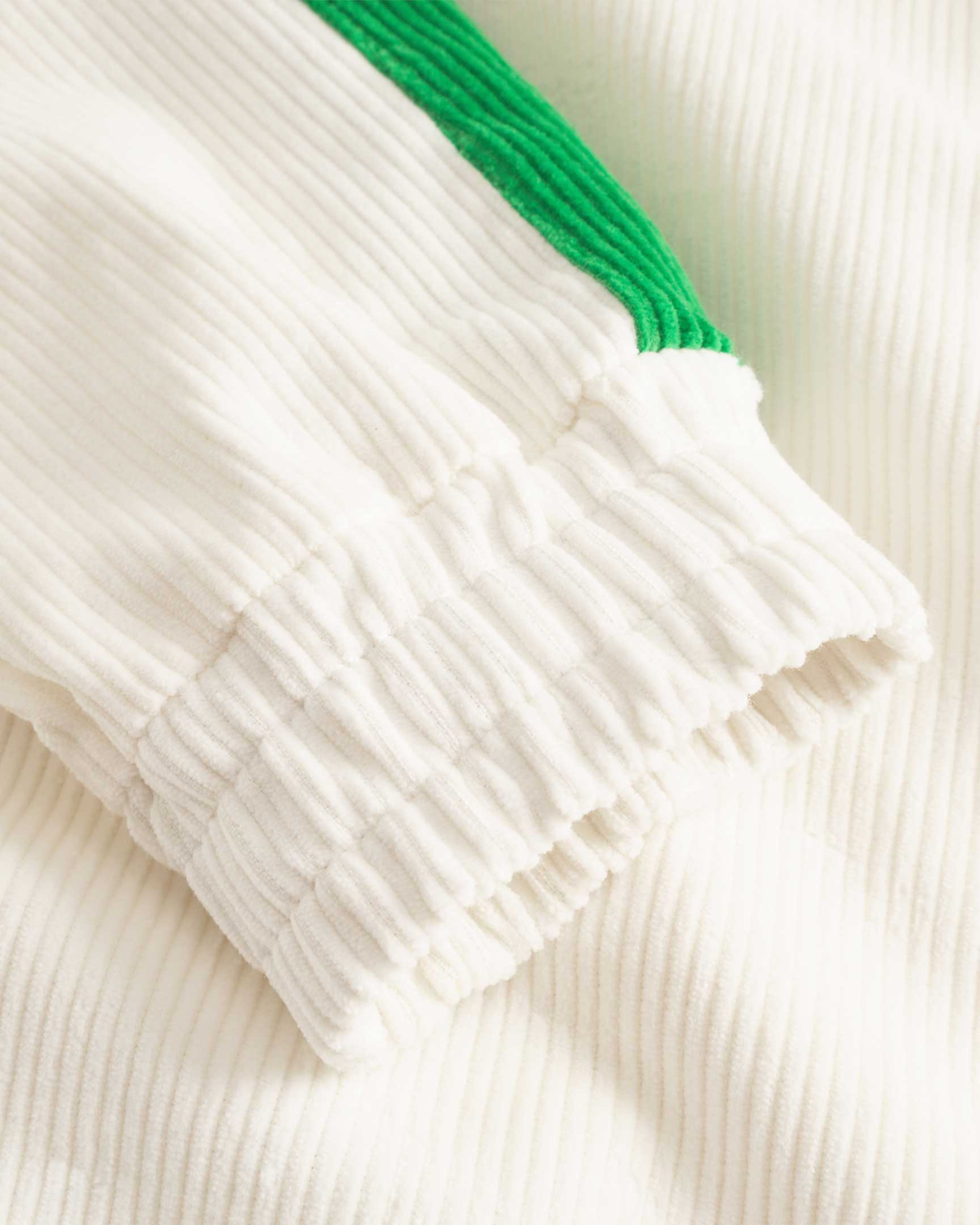 Close up of ribbed cuffs on a white and green corduroy track suit jacket with NB embroidery and full zipper