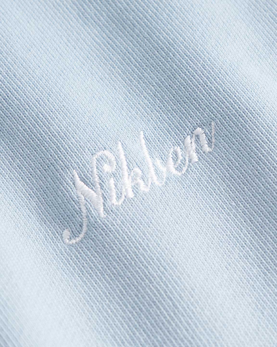 Close up of Niben script embroidery on a baby blue hoodie