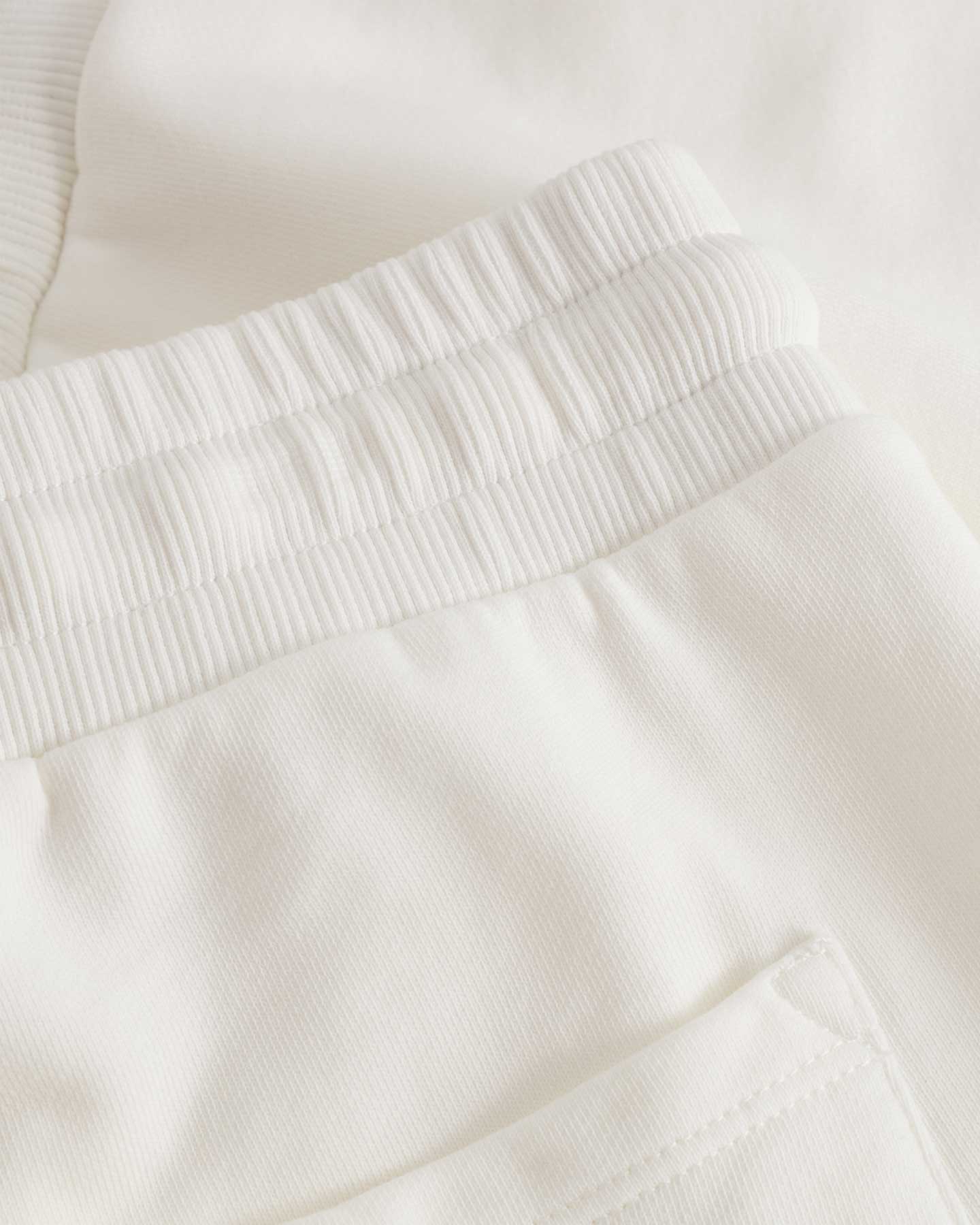 Close up on ribbed waist and back pocket on white jersey shorts with drawstrings and green embroidery