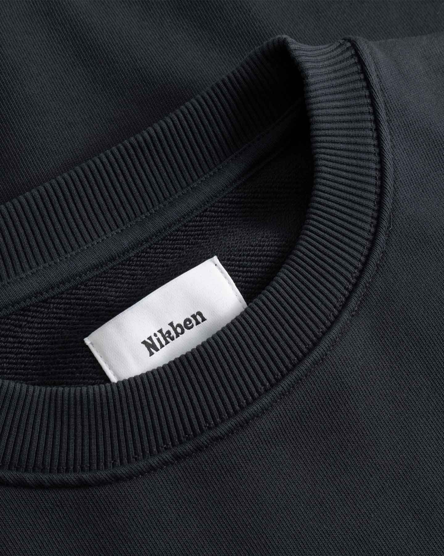 Close-up of a black sweater with a white label displaying 'Nikben' 