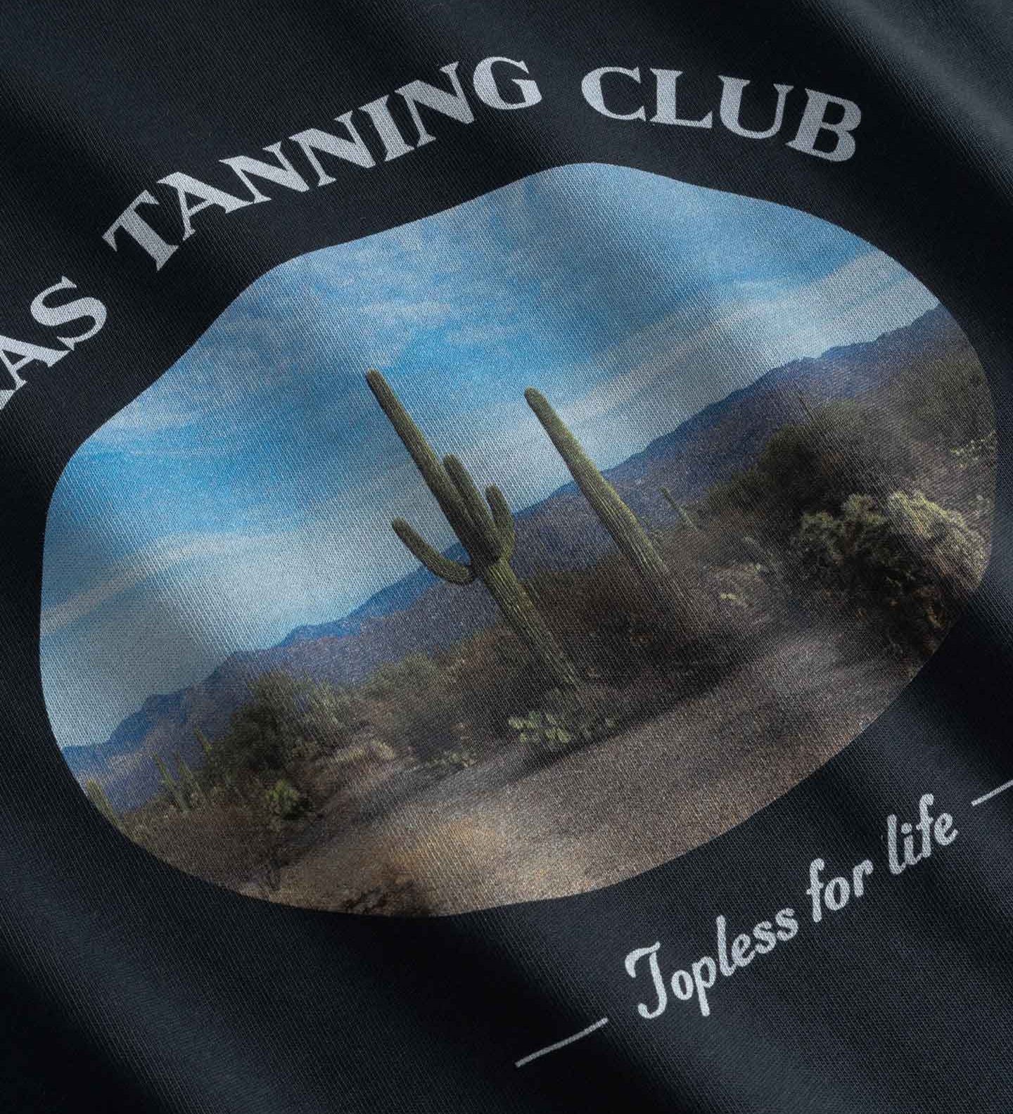Close up of Black t-shirt with desert scene and 'Texas Tanning Club' text 