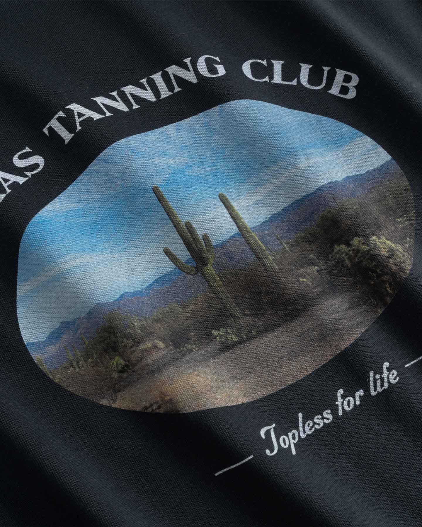 Close up of Black t-shirt with desert scene and 'Texas Tanning Club' text 
