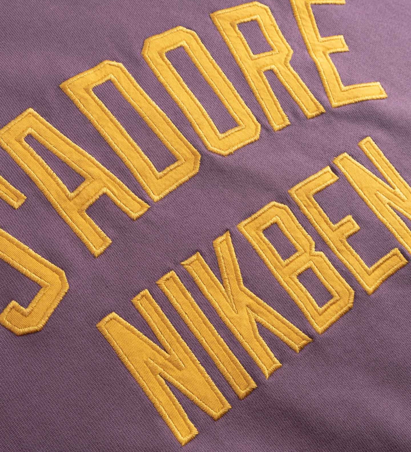 Yellow Text 'I adore NIKBEN' embroidered on a purple fabric.