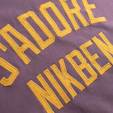 Yellow Text 'I adore NIKBEN' embroidered on a purple fabric.