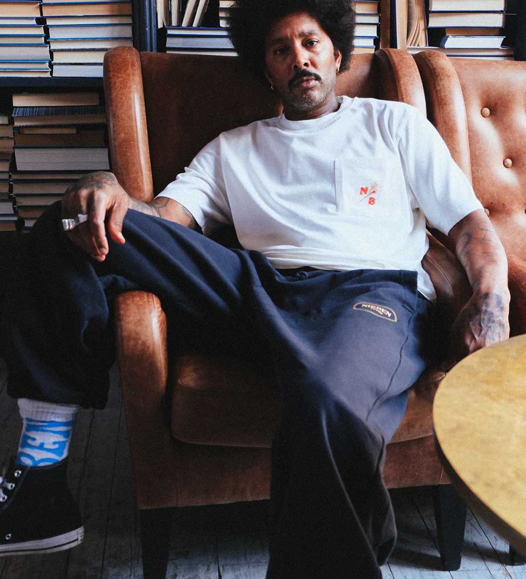 Model sitting wearing black sweat pants logo on thigh