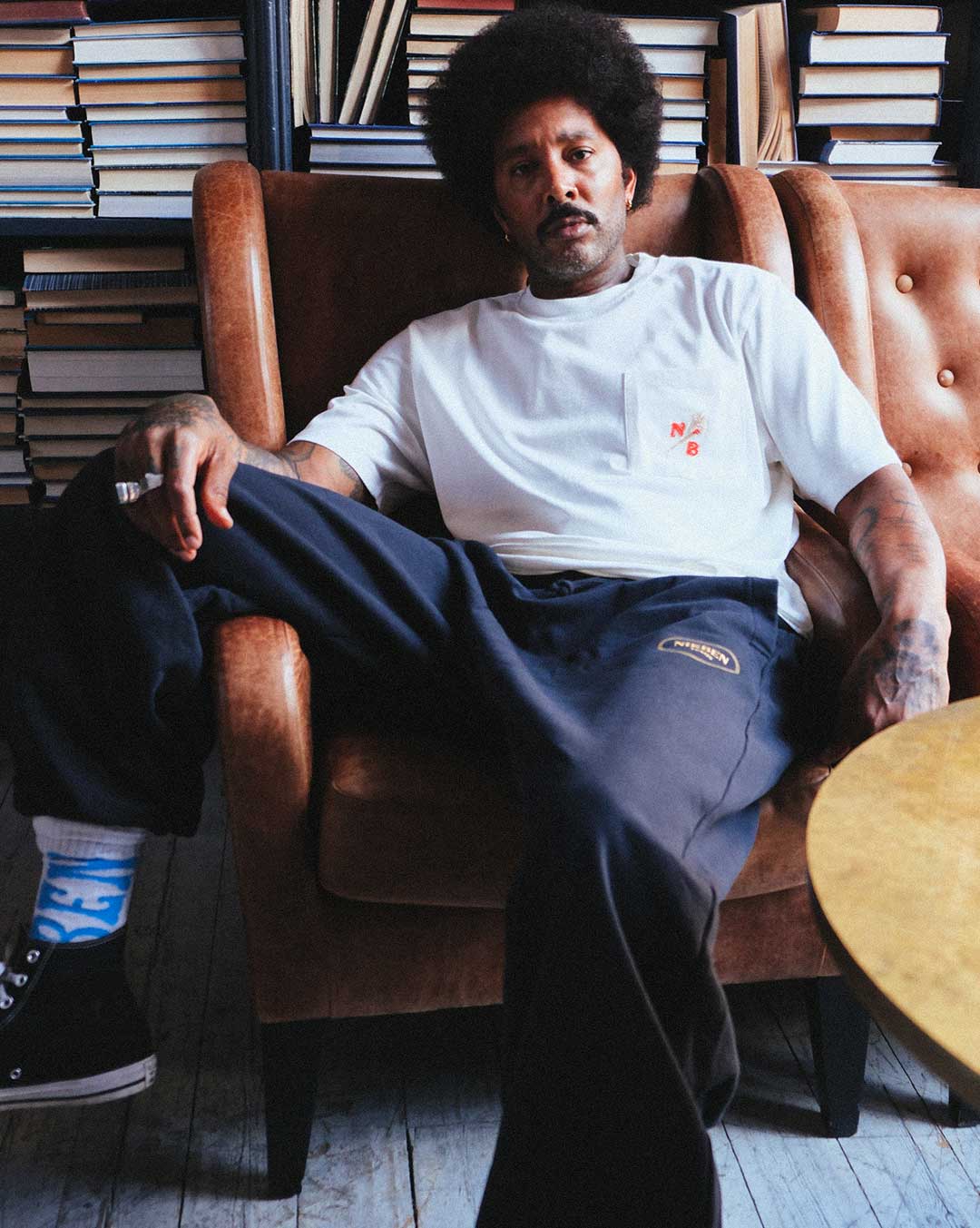 Model sitting wearing black sweat pants logo on thigh