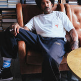 Model sitting wearing black sweat pants logo on thigh