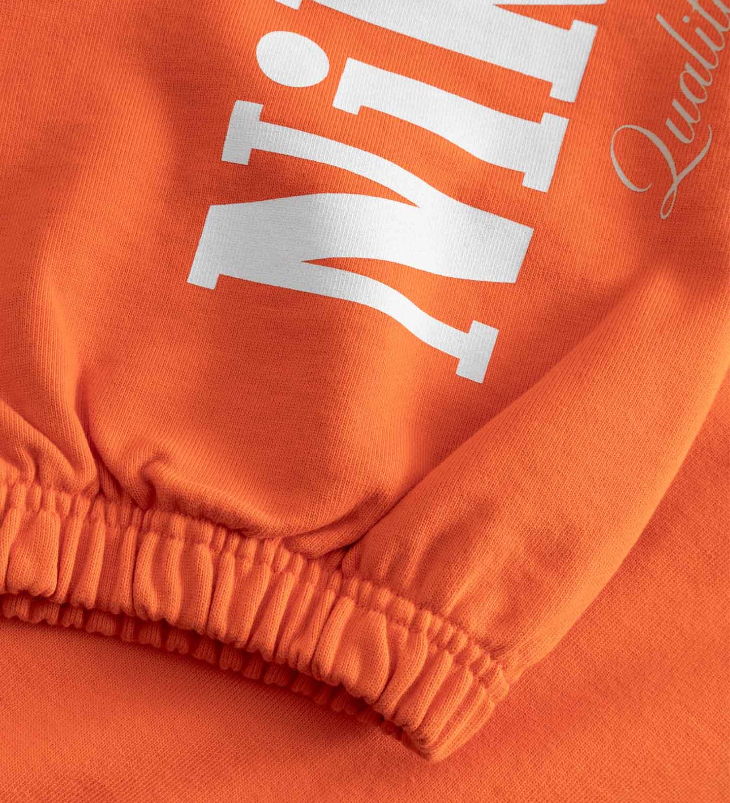 Close-up of an orange sweatshirt with white boldtext on sleeves 