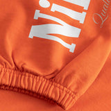 Close-up of an orange sweatshirt with white boldtext on sleeves 