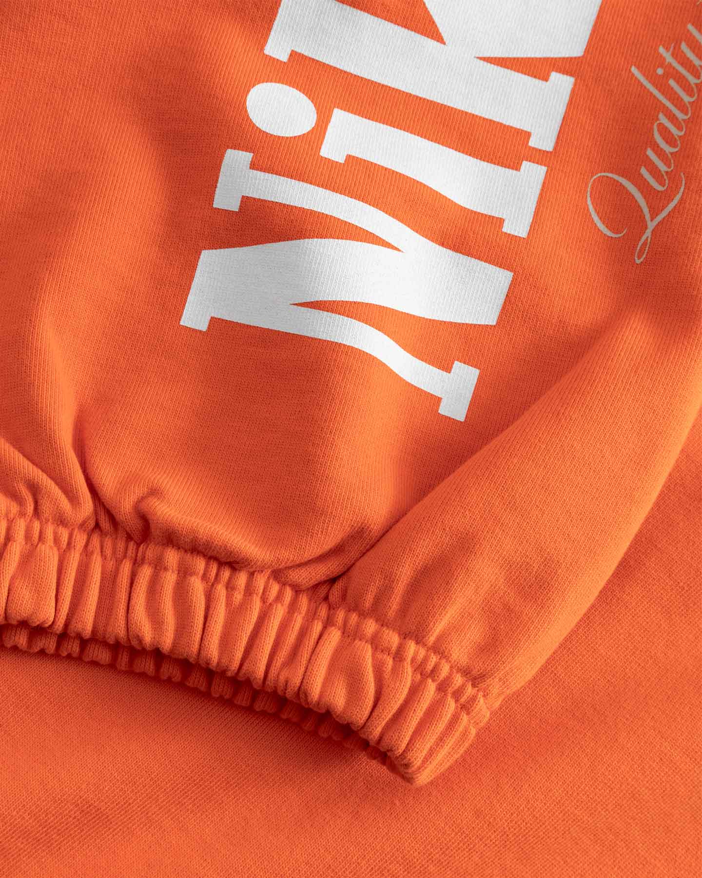 Close-up of an orange sweatshirt with white boldtext on sleeves 