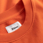 Close-up of an orange sweatshirt with a white label displaying 'Nikben'.