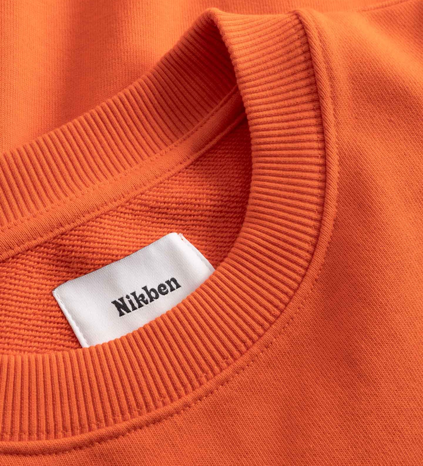 Close-up of an orange sweatshirt with a white label displaying 'Nikben'.