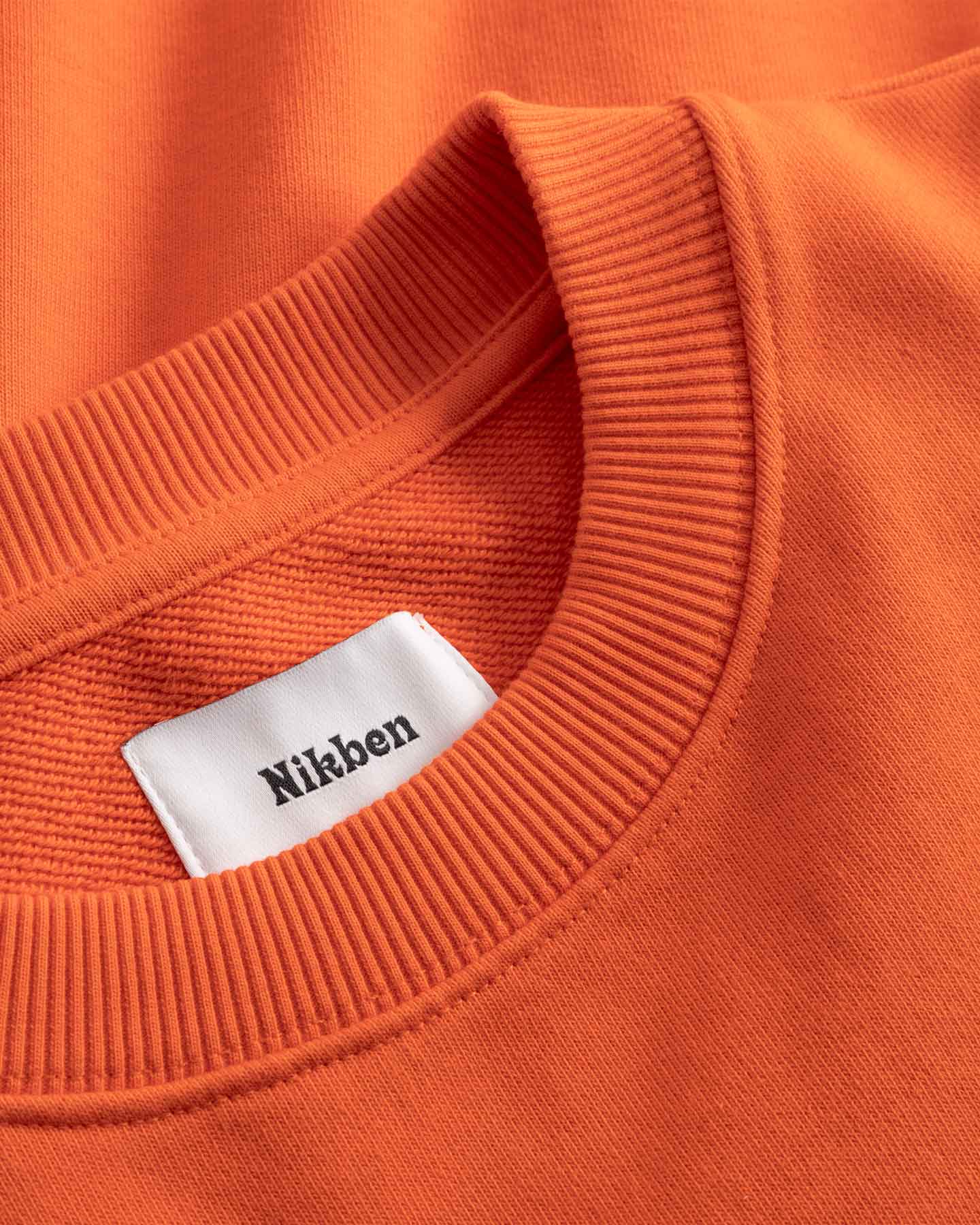 Close-up of an orange sweatshirt with a white label displaying 'Nikben'.