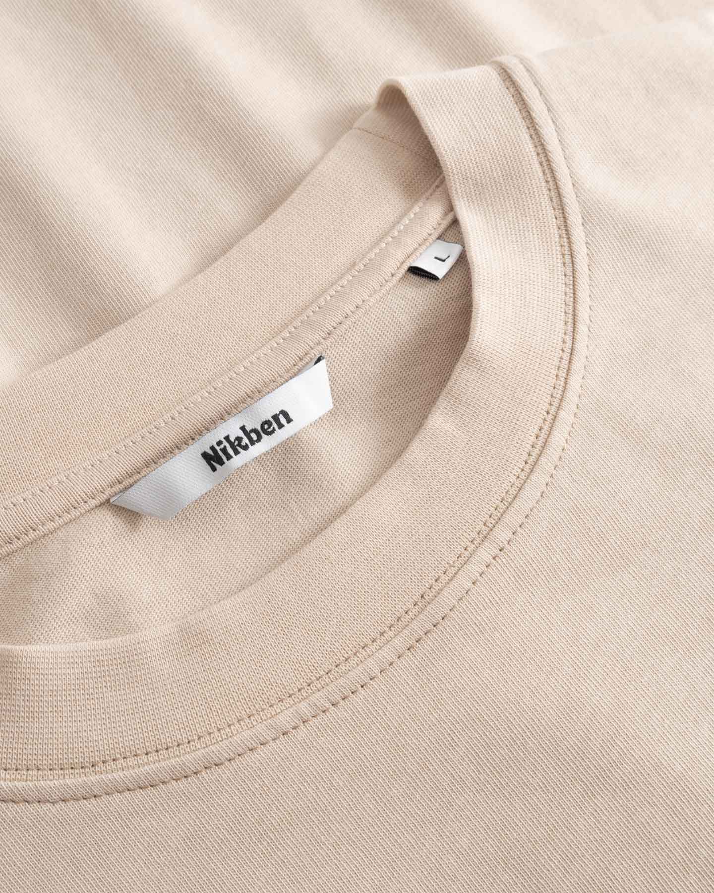 Close-up of a beige t-shirt with a Nikben label on the collar.
