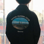 model wearing a black overshirt with 'Texas Tanning Club' logo and desert scene on the back, 