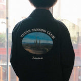 model wearing a black overshirt with 'Texas Tanning Club' logo and desert scene on the back, 