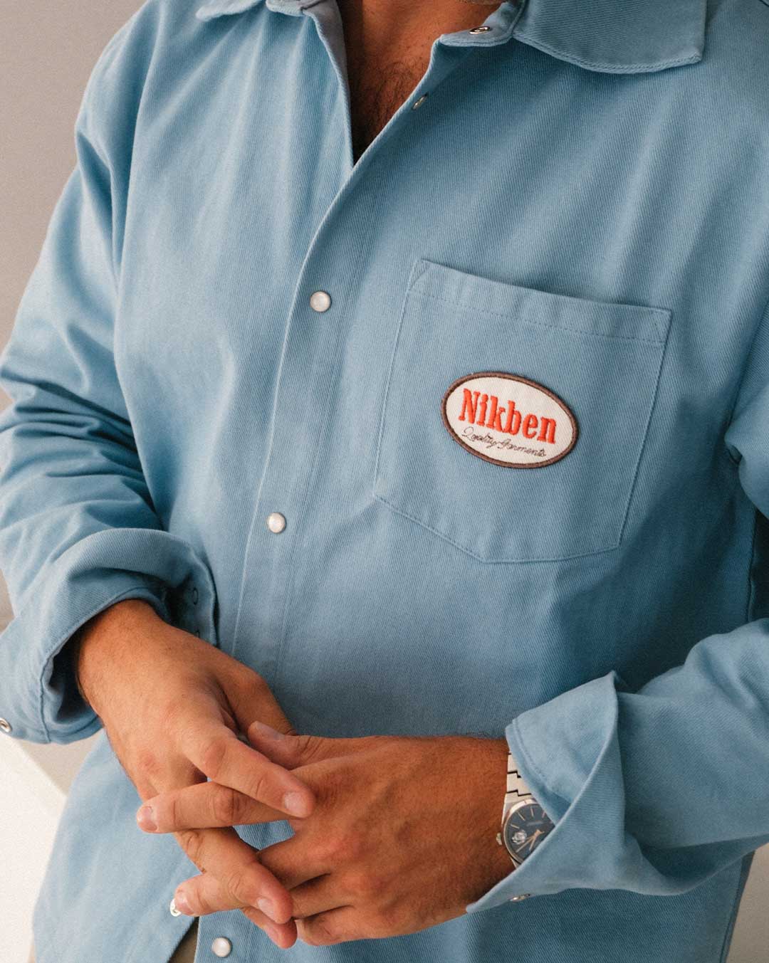 model wearing  blue overshirt with a 'Nikben' logo on breast pocket