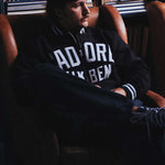 Model wearing a black bomber jacket with white text sitting on a chair