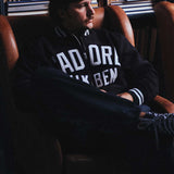 Model wearing a black bomber jacket with white text sitting on a chair