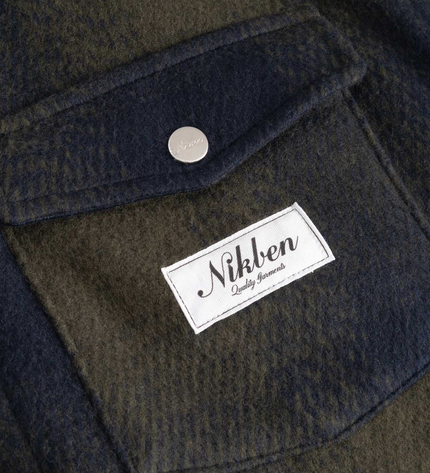 Close up on dark blue and green flannel overshirt front breast pocket with Nikben brand logo