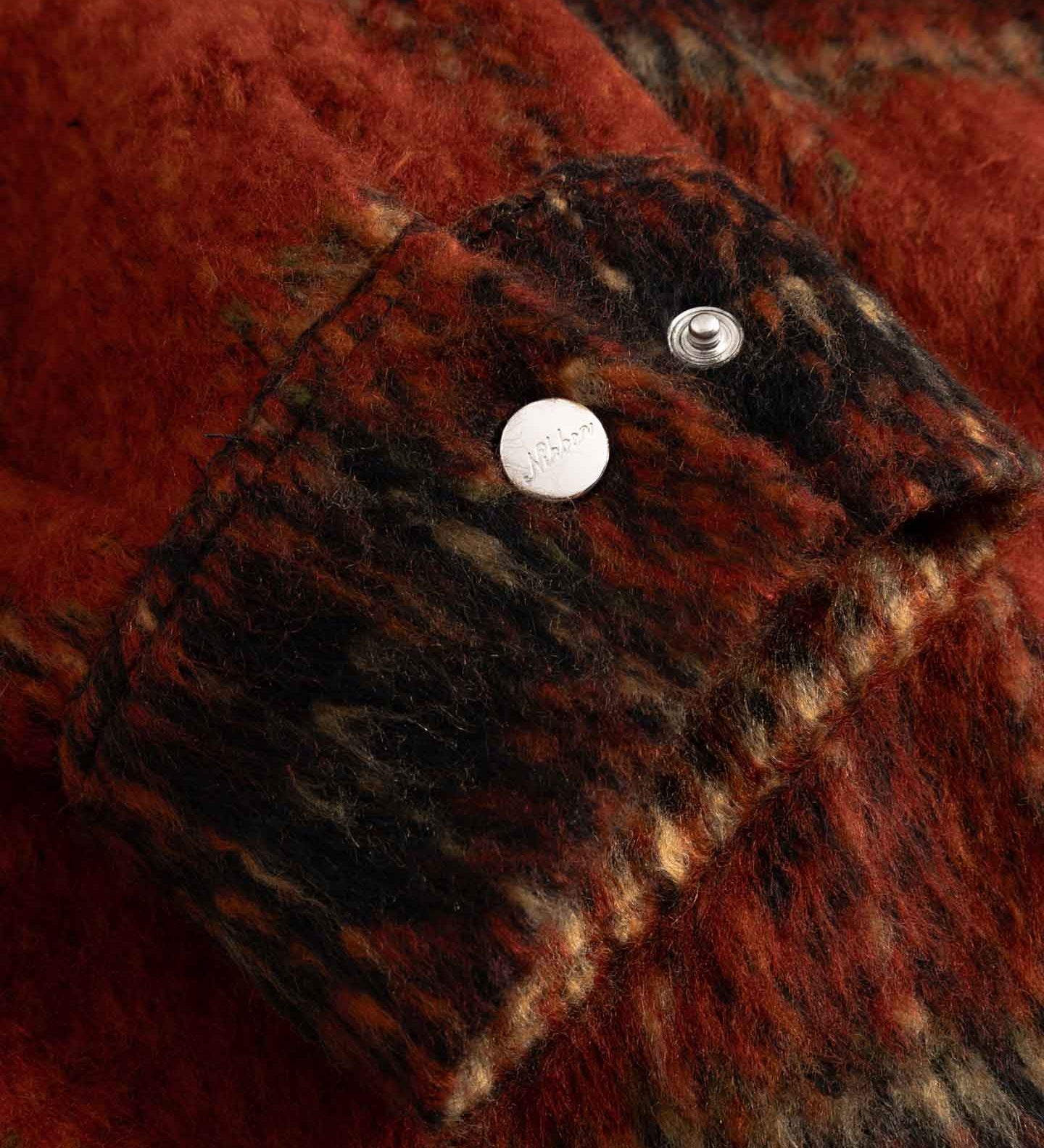 Close-up of red and black textured fabric on sleeve cuff with silver button detail