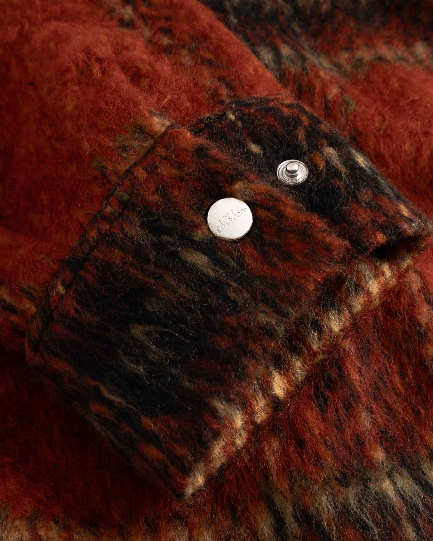 Close-up of red and black textured fabric on sleeve cuff with silver button detail