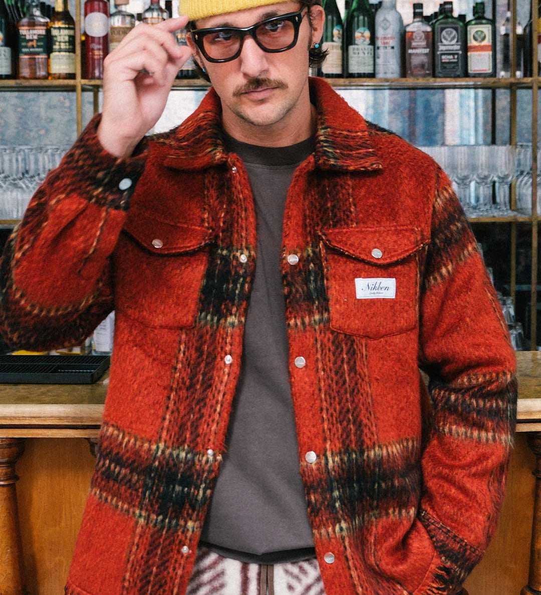 Model wearing a red plaid overshirt open with front breast button down pockets