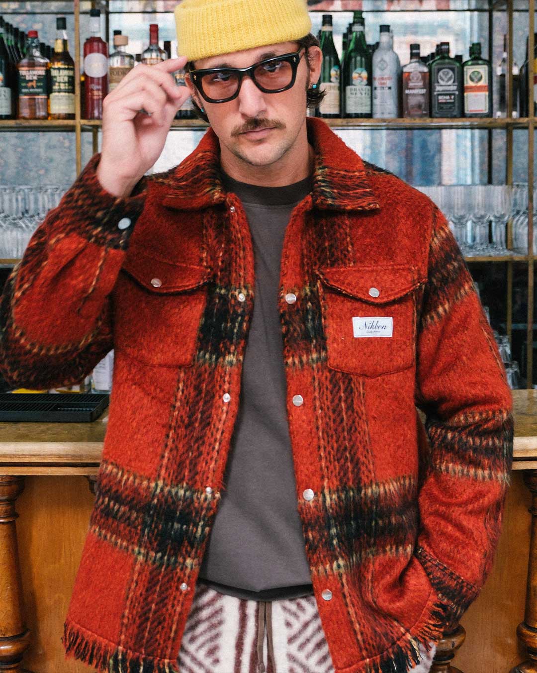 Model wearing a red plaid overshirt open with front breast button down pockets