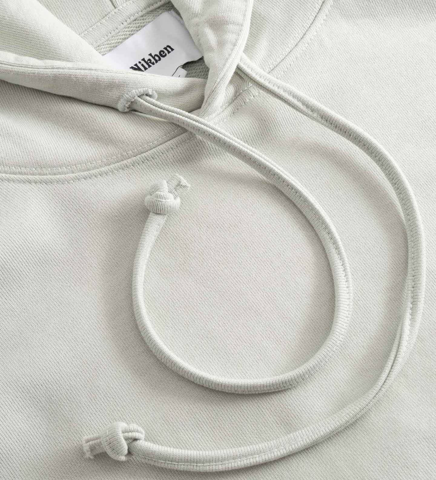 Close-up of beige hoodie with a brand label on the hood and drawstrings.