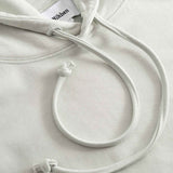 Close-up of beige hoodie with a brand label on the hood and drawstrings.