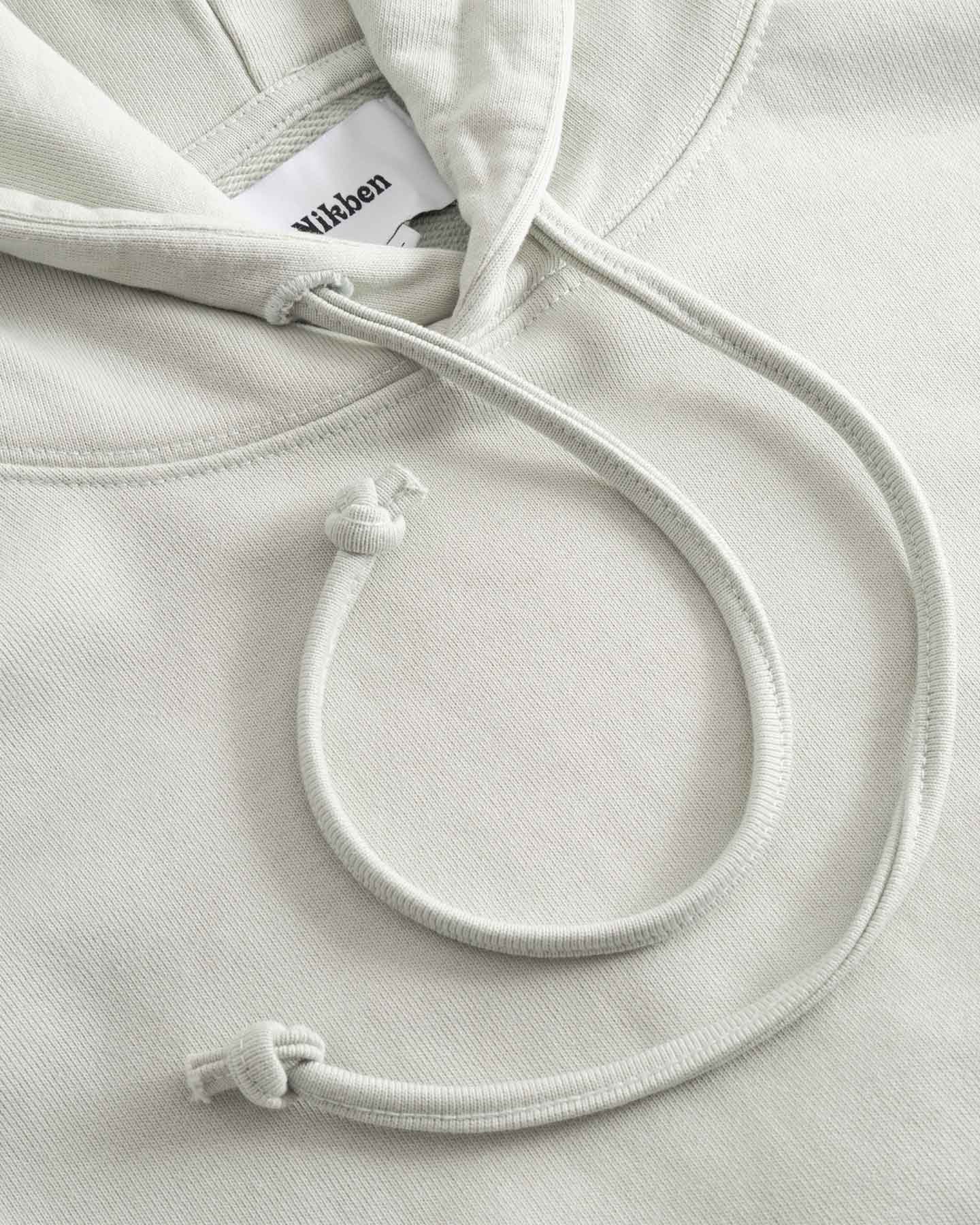 Close-up of beige hoodie with a brand label on the hood and drawstrings.
