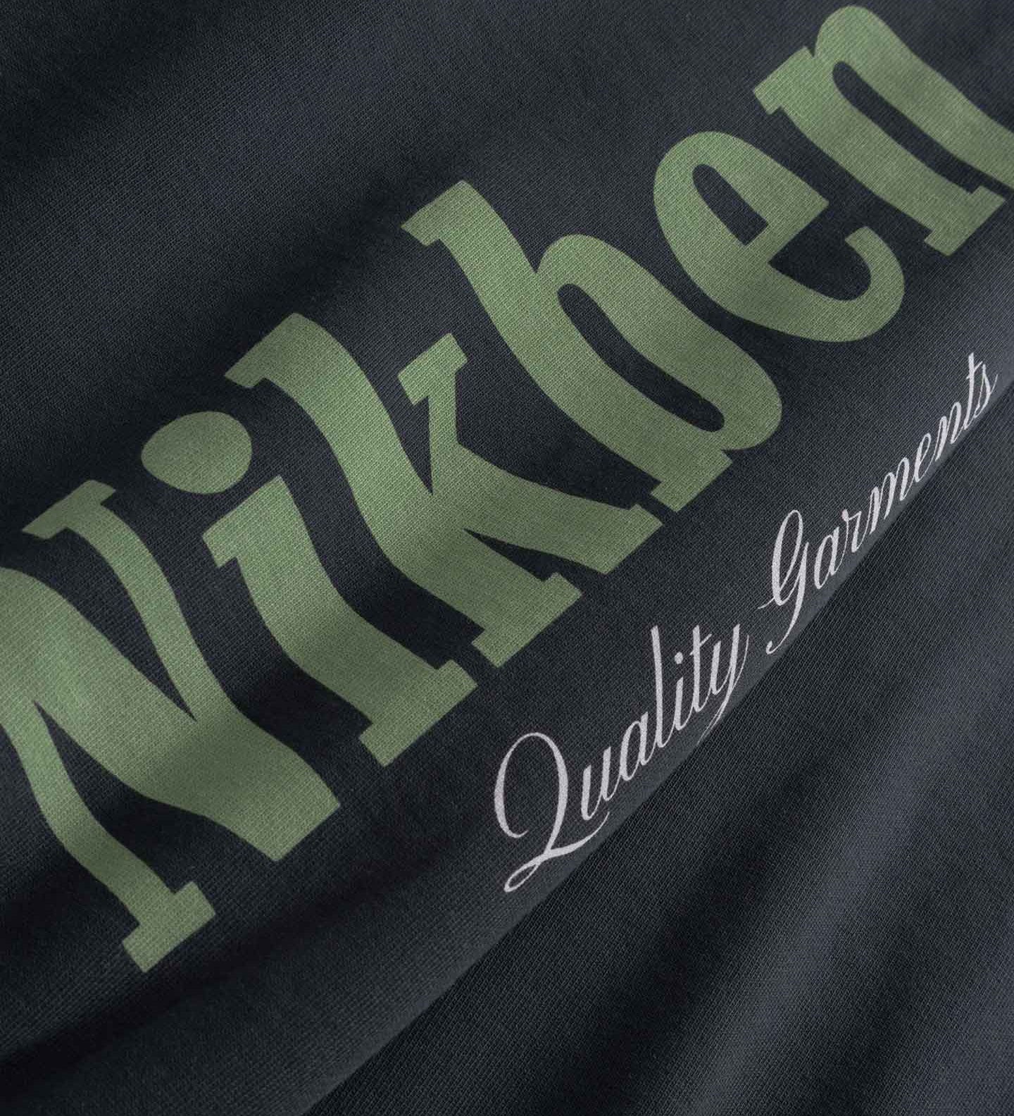 Close up of Black fabric with green and white text 'Nikben' and 'Quality Garments'
