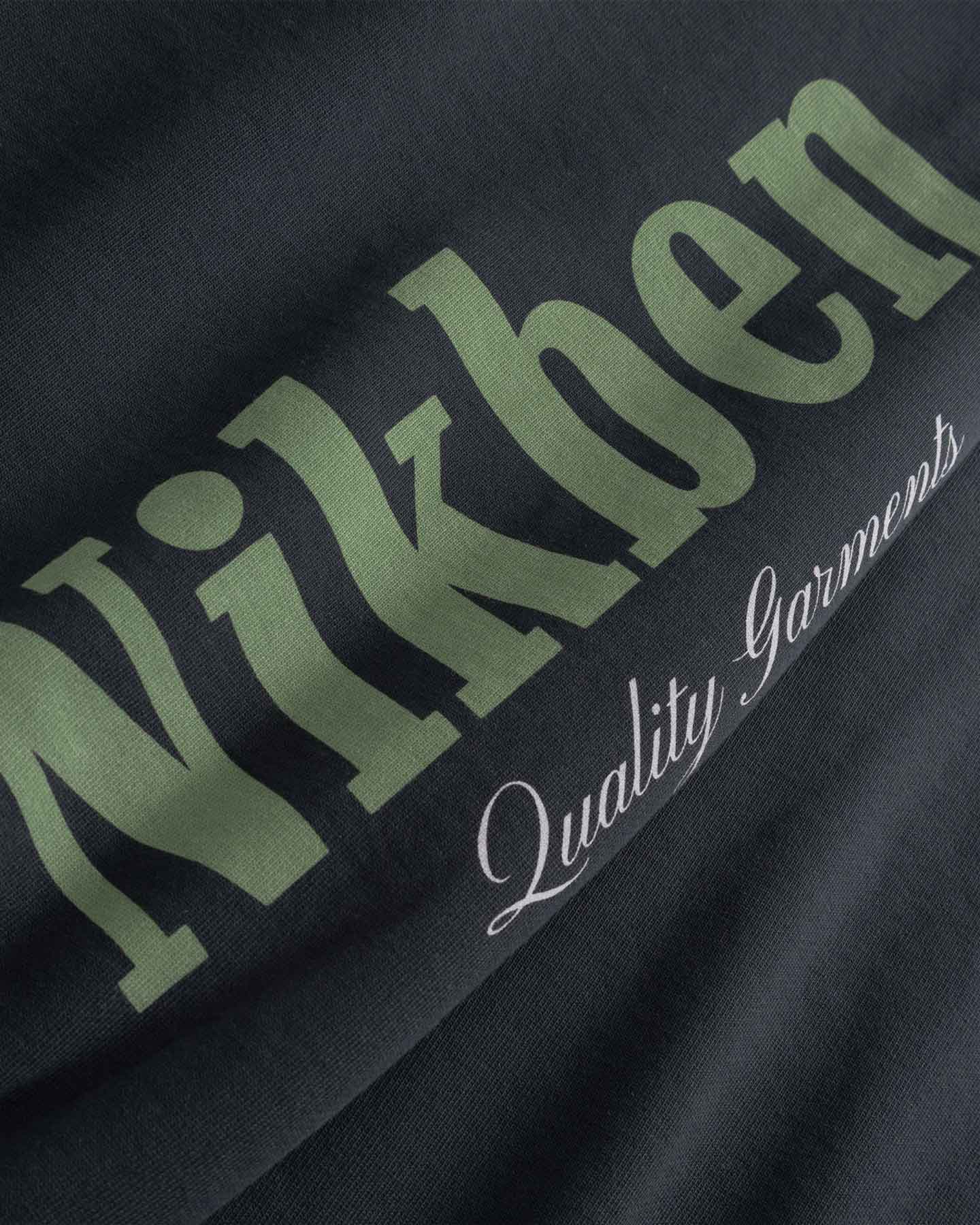 Close up of Black fabric with green and white text 'Nikben' and 'Quality Garments'