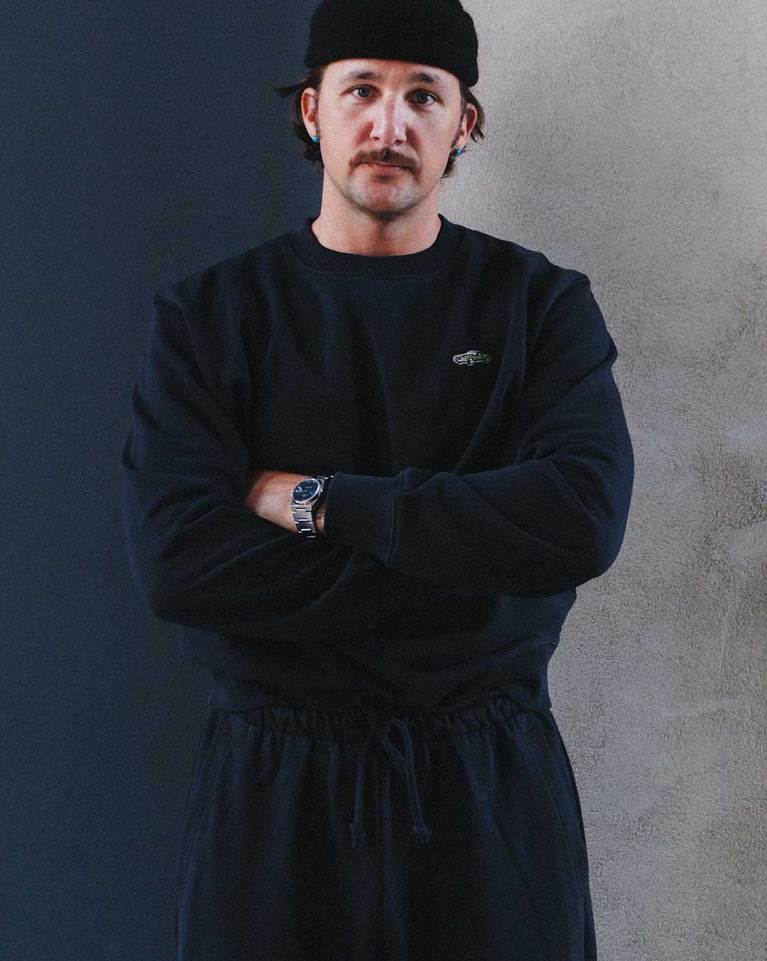 Model wearing a black sweatshirt and pants with a logo on chest.