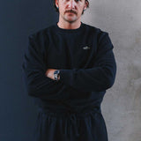 Model wearing a black sweatshirt and pants with a logo on chest.