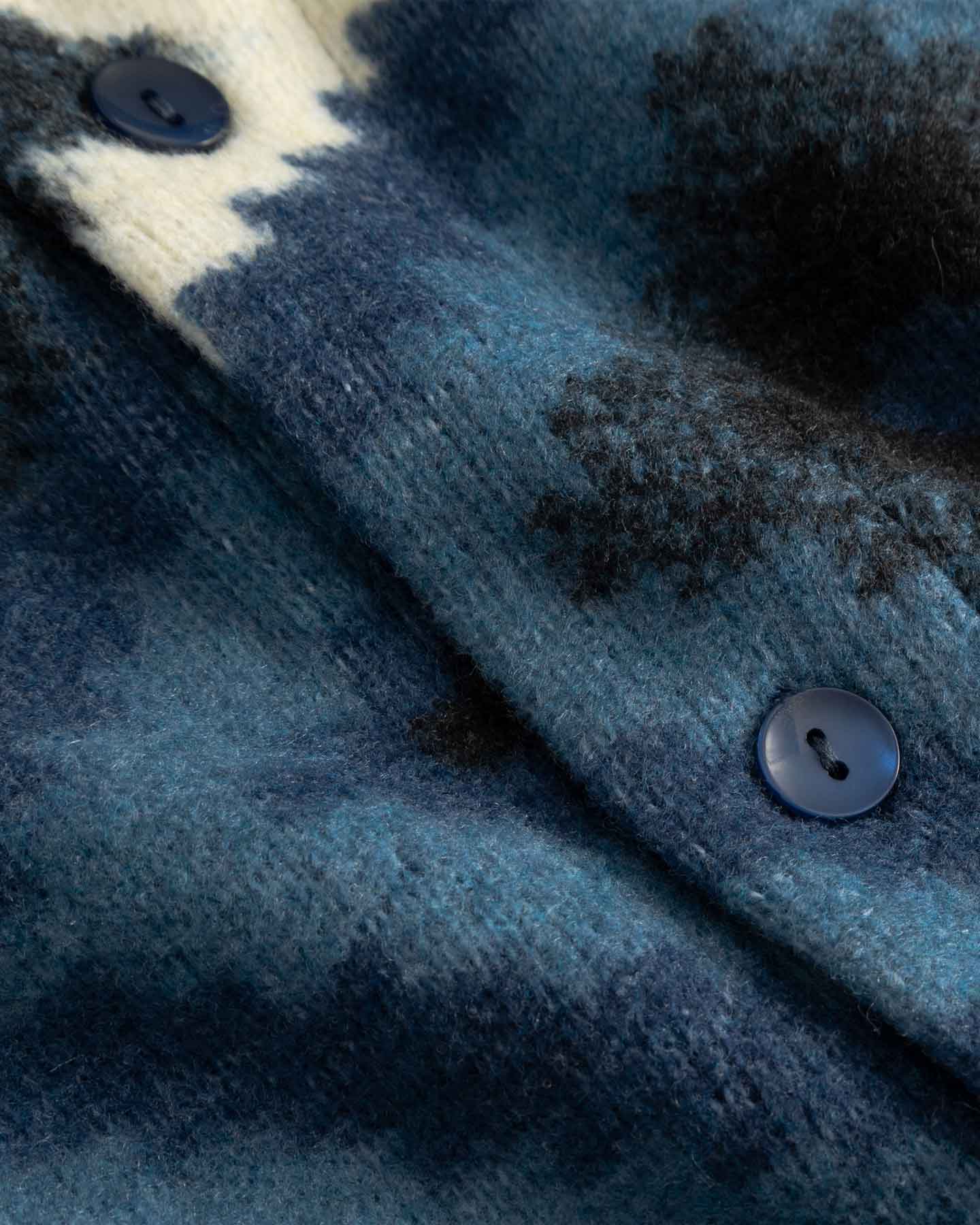 Close-up of textured fabric with buttons on a blue and black diamond Ikat patterned cardigan