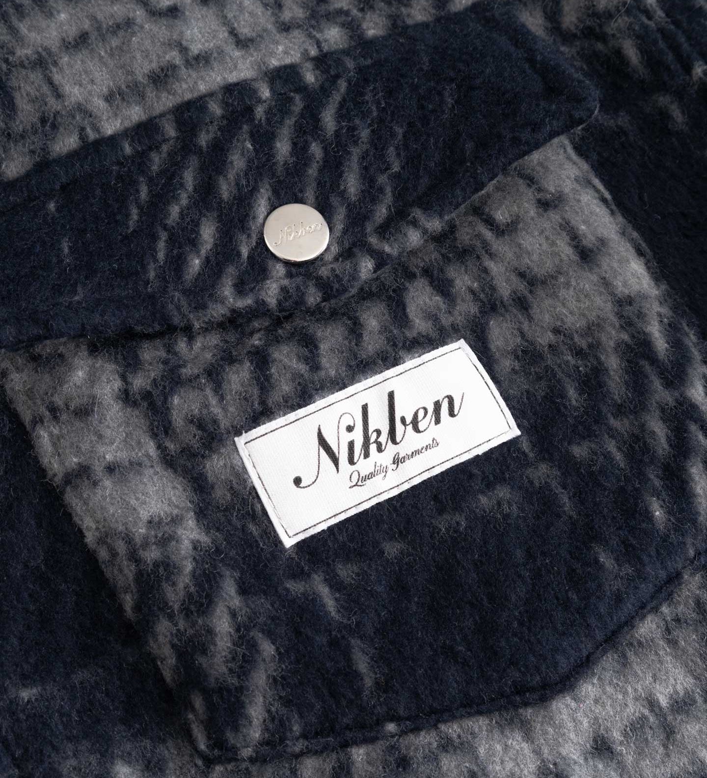 Close up of front chest pocket and logo on navy checkered shirt 

