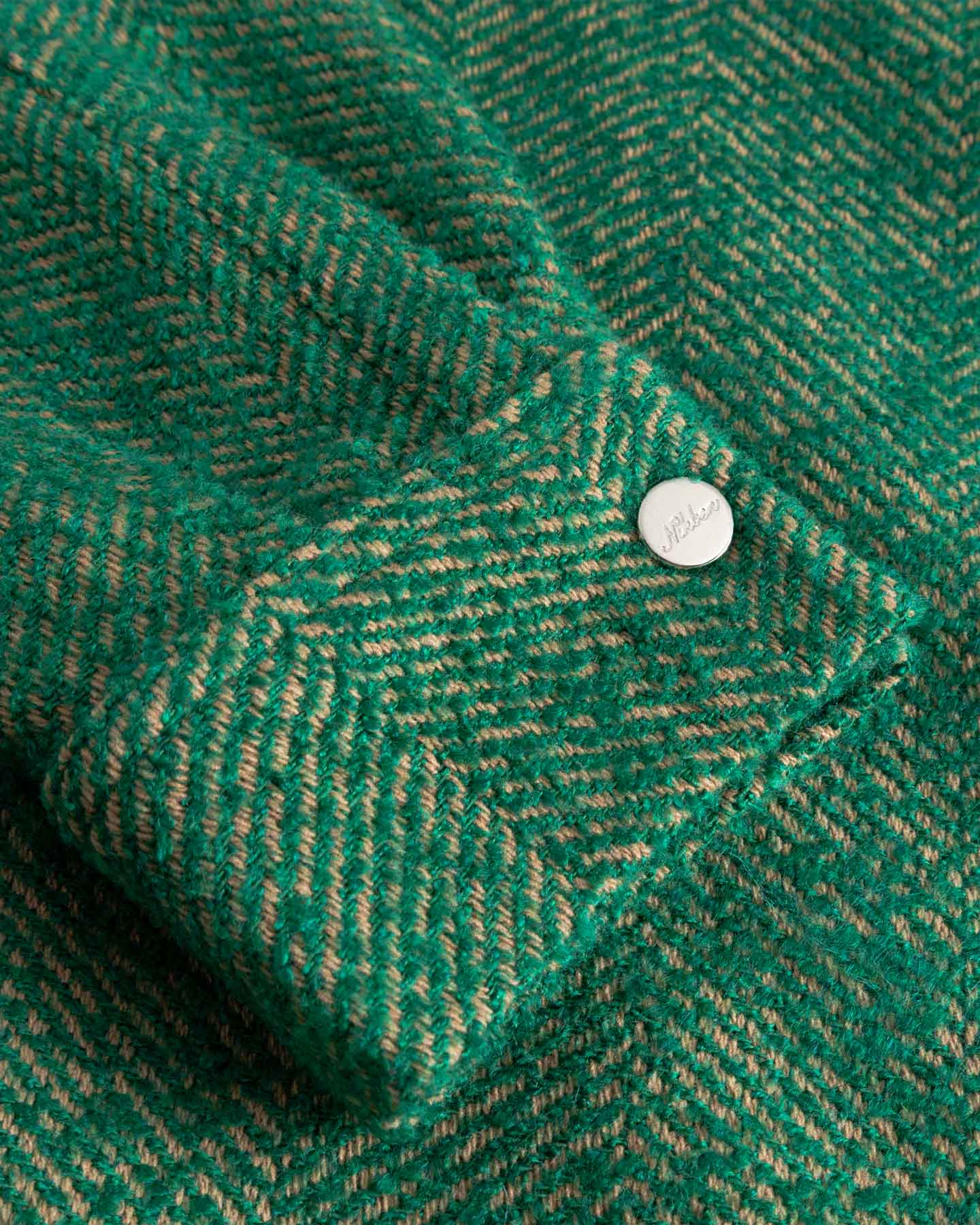 Close-up of a green textured fabric on the cuff with a button down button.