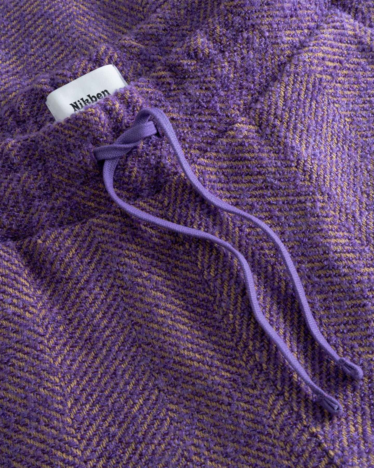 Close-up of a purple textured fabric with a drawstring and visible brand label.