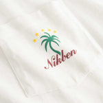 Closeup view of green palm print and red NIKBEN logo on front pocket of white t-shirt