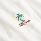 Closeup view of green palm print and red NIKBEN logo on front pocket of white t-shirt