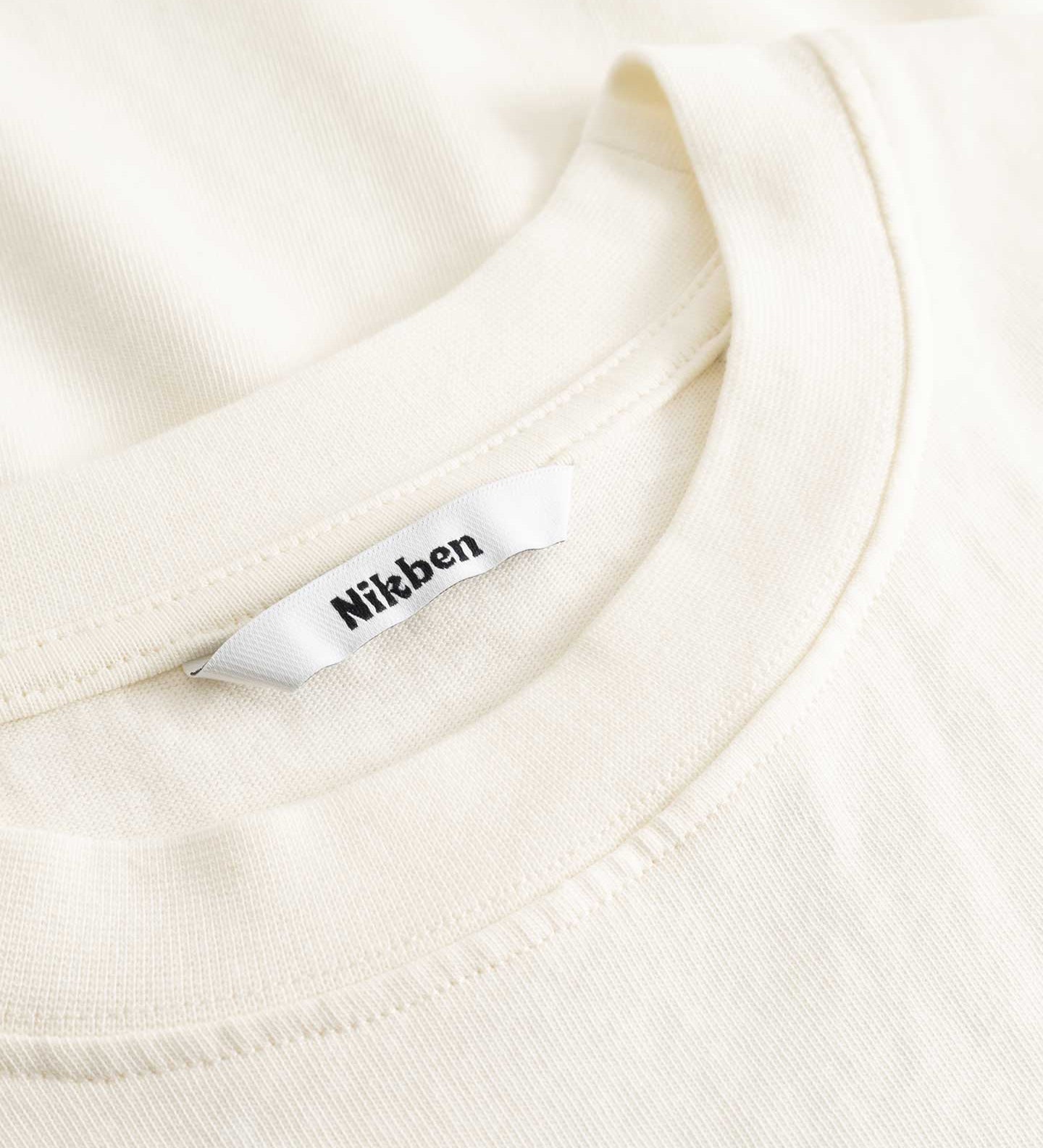 Closeup view of Nikben necklabel on cream colored T-shirt