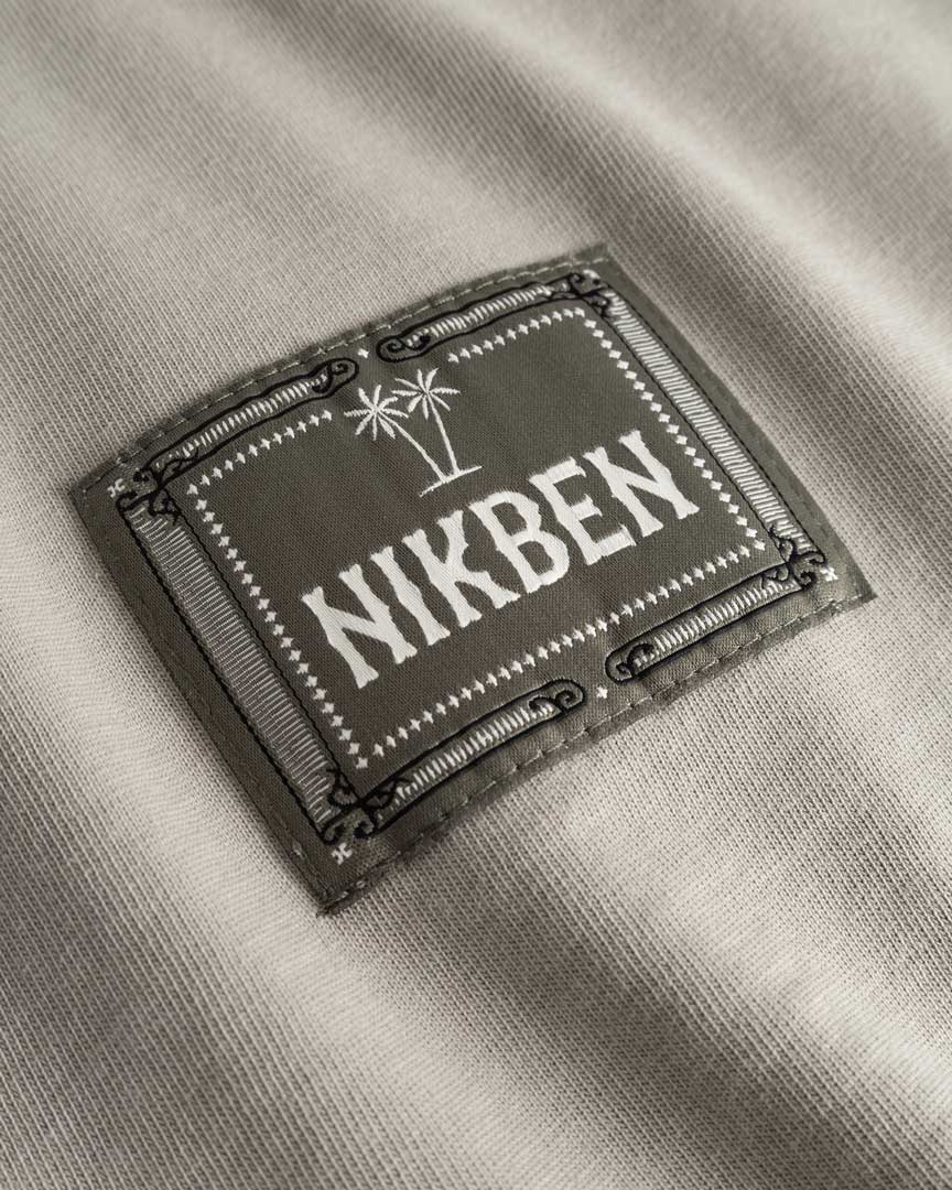 Closeup view of green Nikben patch logo on beige T-shirt