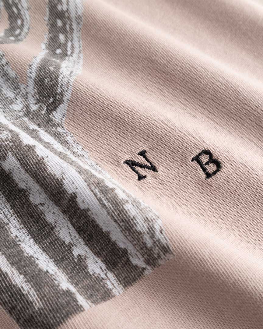 Closeup view of white embroidered NB initials next to cactus print on beige T-shirt